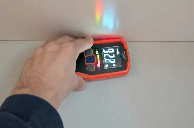 A hand holds a digital moisture meter against a wall during moisture checks