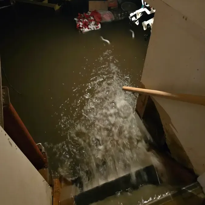 Water rushes down interior basement stairs toward a flooded room and stored belongings