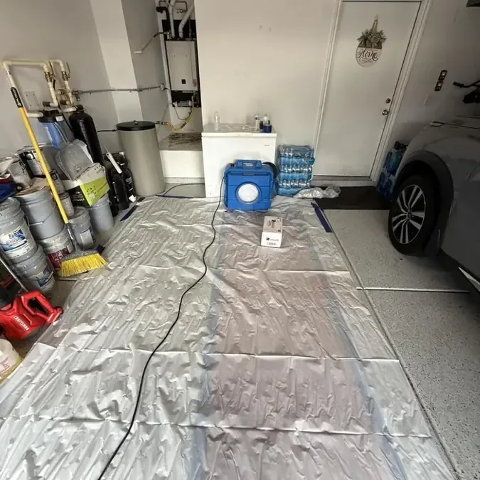 Drying equipment and protective floor sheeting fill a garage beside stored household equipment
