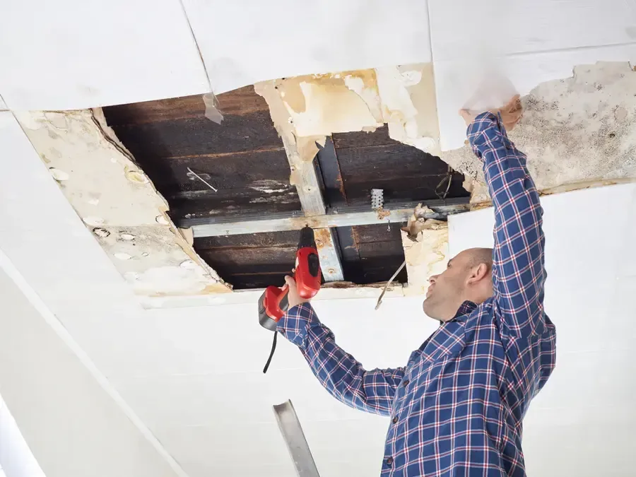 A worker cuts damaged ceiling drywall to expose overhead framing around water stains