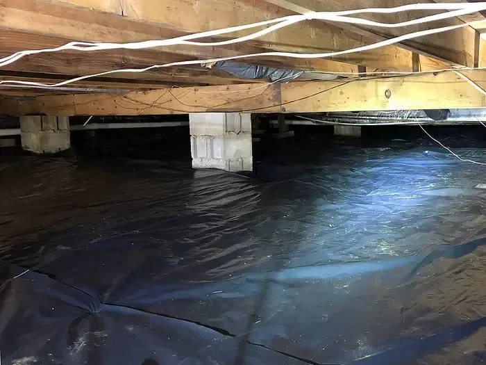 Water collects over a crawl space liner beneath exposed joists and support piers