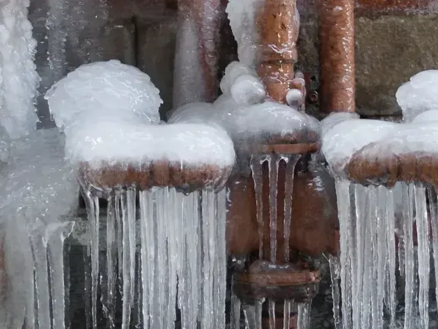 Thick ice and hanging icicles cover copper pipes and joints during freezing conditions